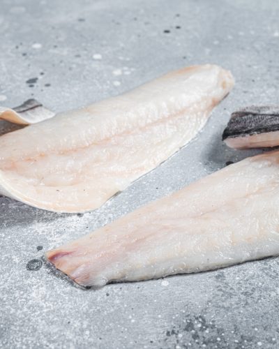 Two raw haddock fish fillets on kitchen table. Gray background. Top view.
